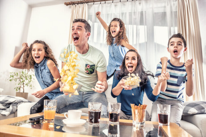 Raving fans cheering sports, as family of five watch football, or ice-hockey match on the TV at home, screaming from joy. Game Day hosting essentials